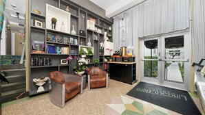 Um hall de hotel moderno com uma grande estante de livros, poltronas de couro e um balcão de recepção.