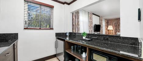 A modern kitchen with a black countertop, a built-in microwave, and a stainless steel refrigerator.