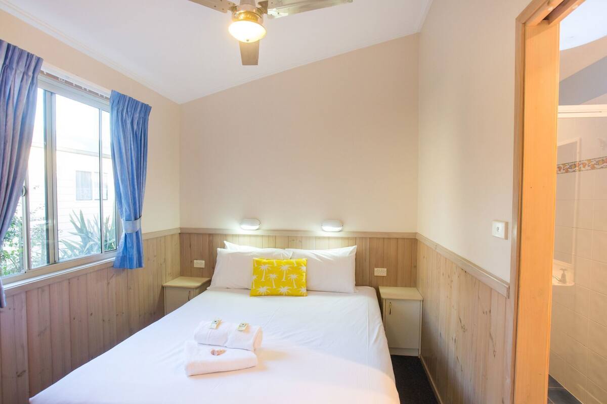 Ein Hotelzimmer mit einem Bett, zwei Nachttischen, einem Deckenventilator und einem Fenster mit Vorhängen.