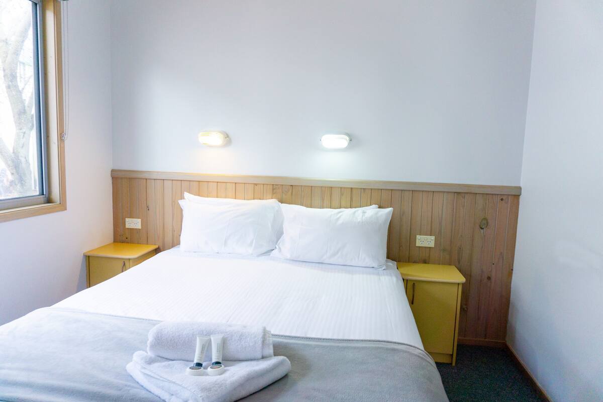 Ein Hotelzimmer mit einem Bett, zwei Nachttischen, einem Fenster und zwei Wandleuchten.
