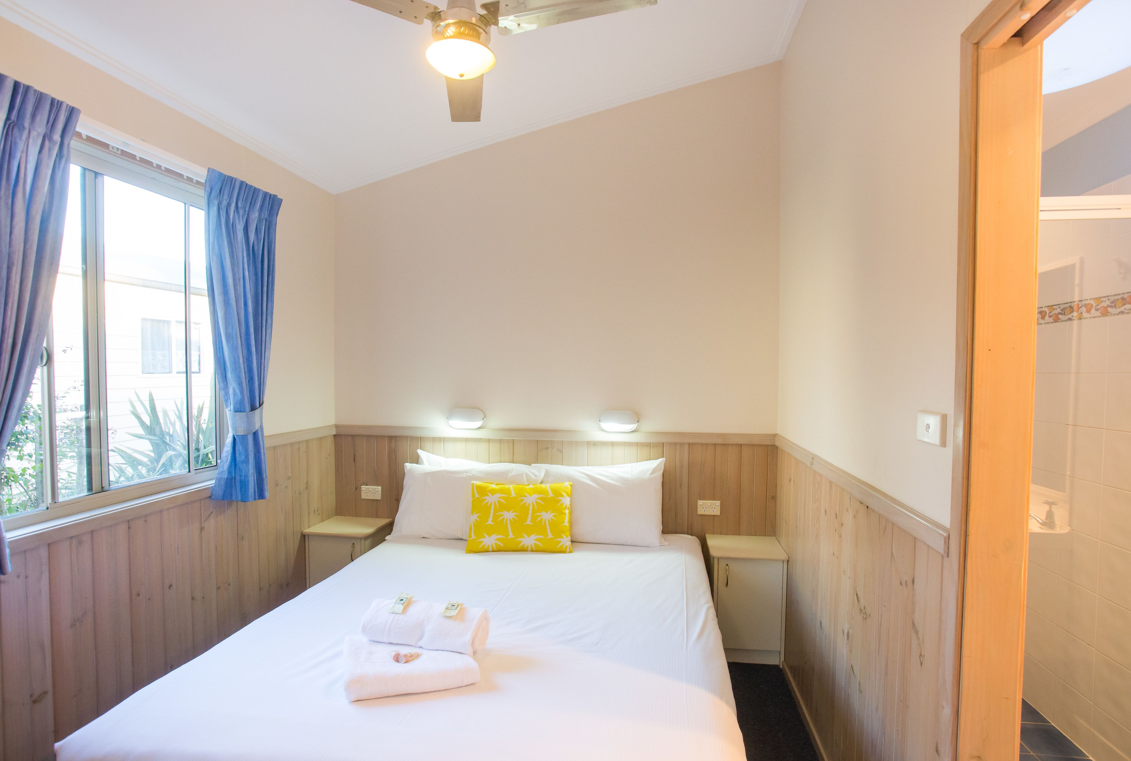 A hotel room with a bed, a nightstand, a window with curtains, and a ceiling fan.