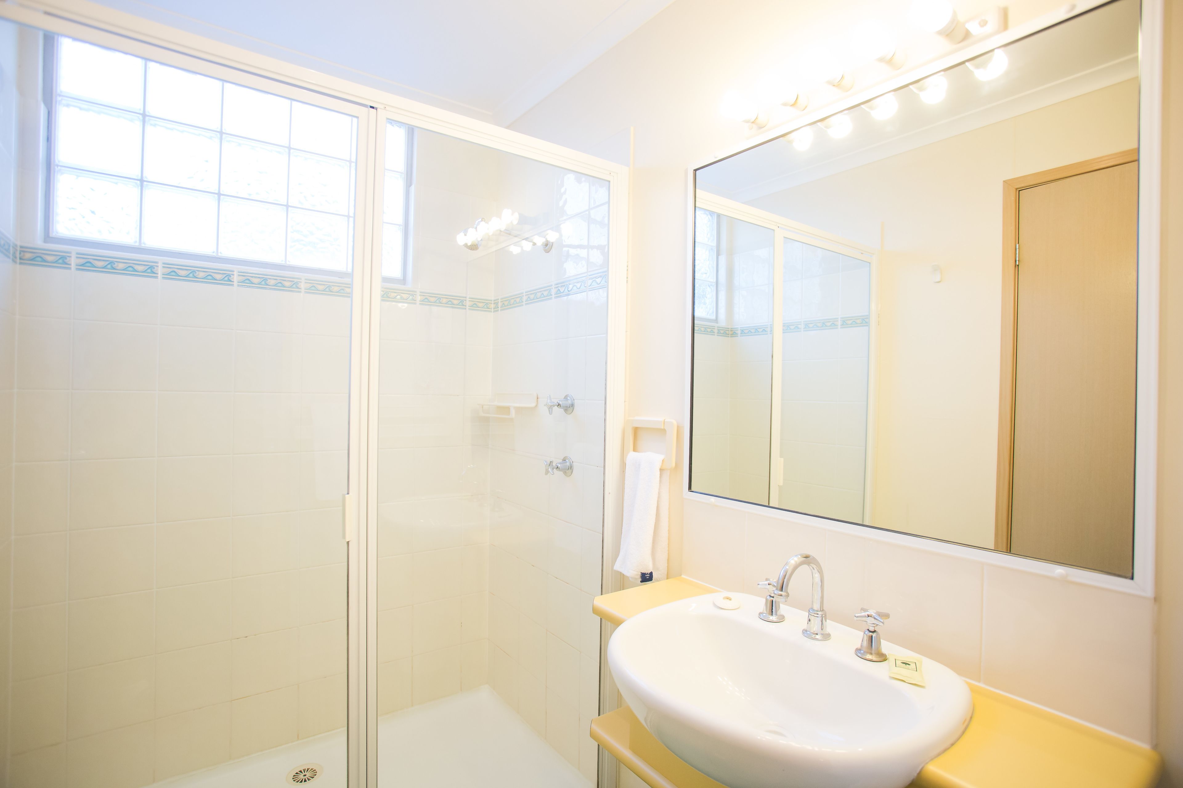 Une salle de bain avec une douche à parois de verre, un lavabo avec un miroir et un porte-serviettes.