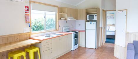A compact kitchen with a window, a microwave, a stove, and two yellow stools.