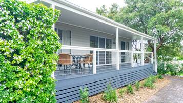 A house with a covered porch, a dining area with chairs, and a small garden area with plants and mulch.