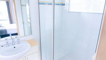 A bathroom with a white sink, a mirror, and a glass shower enclosure.