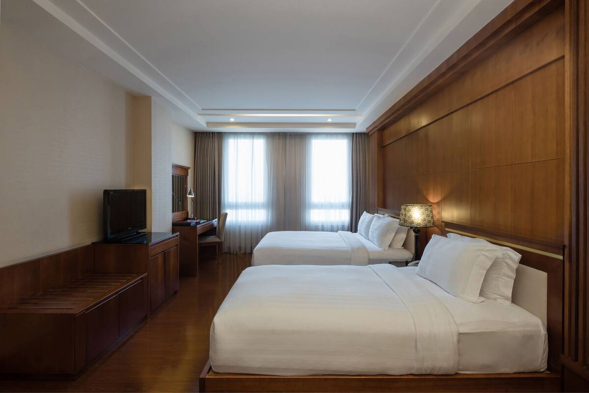 A hotel room with two beds, a desk, a television, and a lamp.