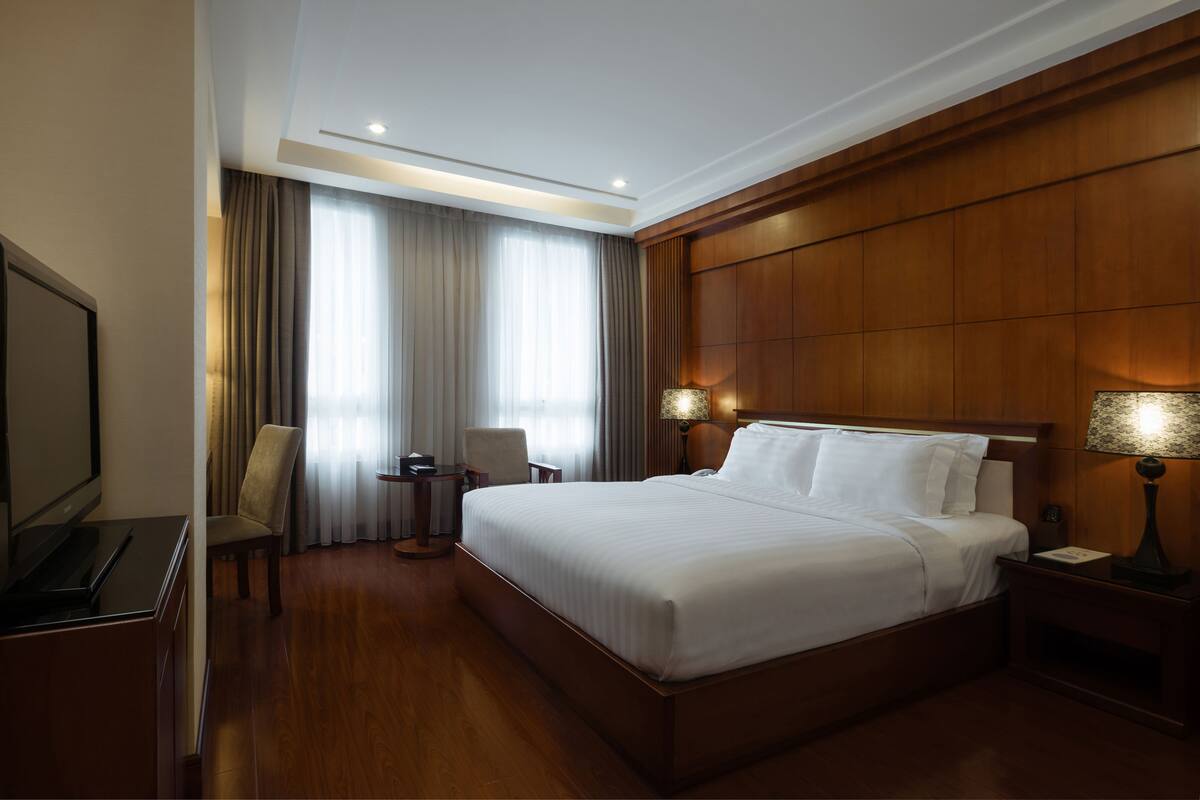 A hotel room with a large bed, a television, a desk, and a chair.