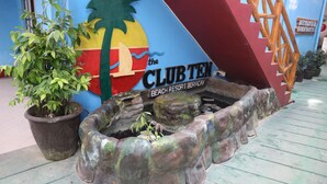 Ein dekorativer Pflanztopf mit einer kleinen Pflanze, ein Wandgemälde mit Palmen und ein Schild für 'The Club Ten Beach Resort Boracay'.