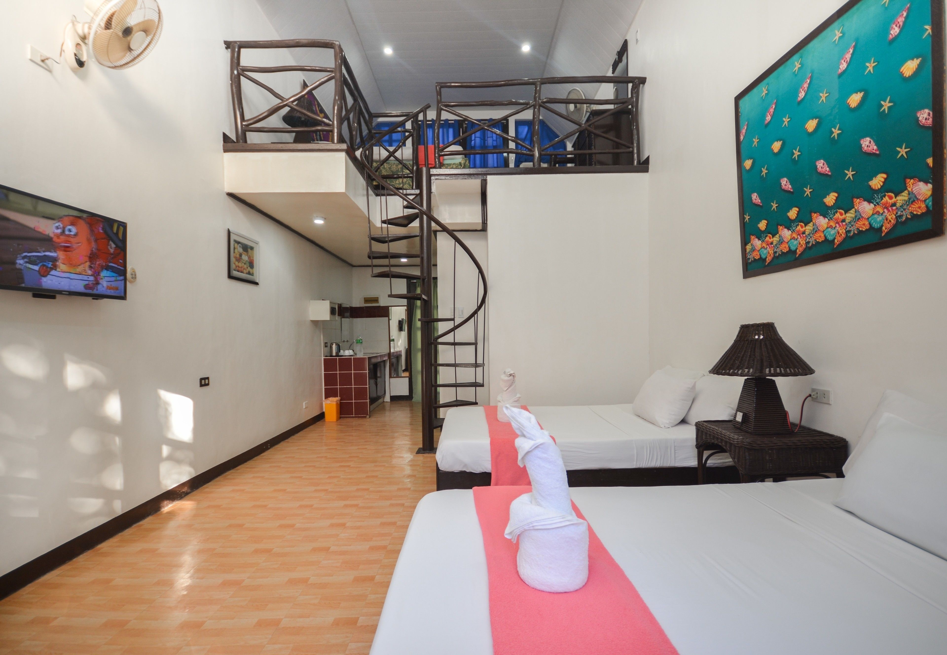 A hotel room with a bed, a small table with a lamp, a painting on the wall, a TV, and a staircase leading to an upper level.