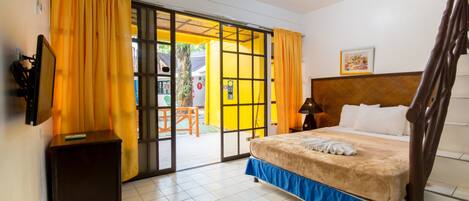 A bedroom with a bed, curtains, a TV, and a sliding door to a balcony.