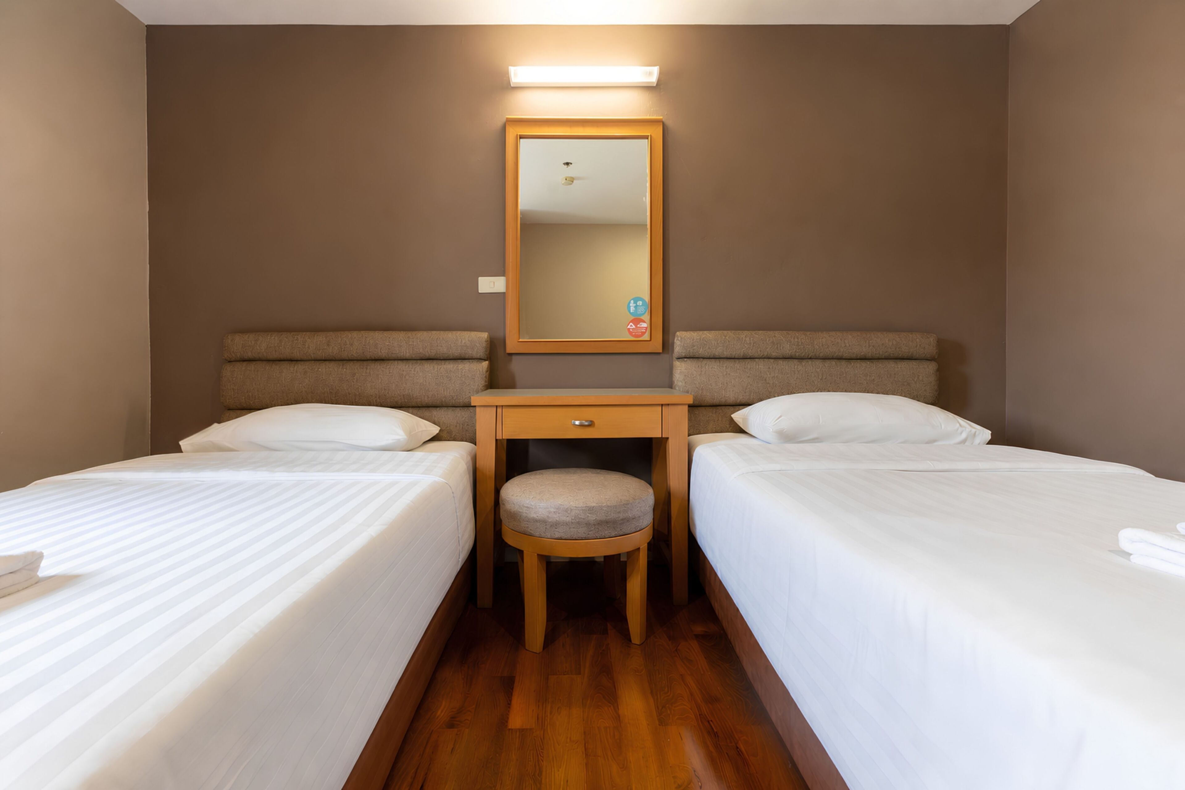 Habitación de hotel con dos camas, un escritorio pequeño con una silla, un espejo y una lámpara sobre el espejo.