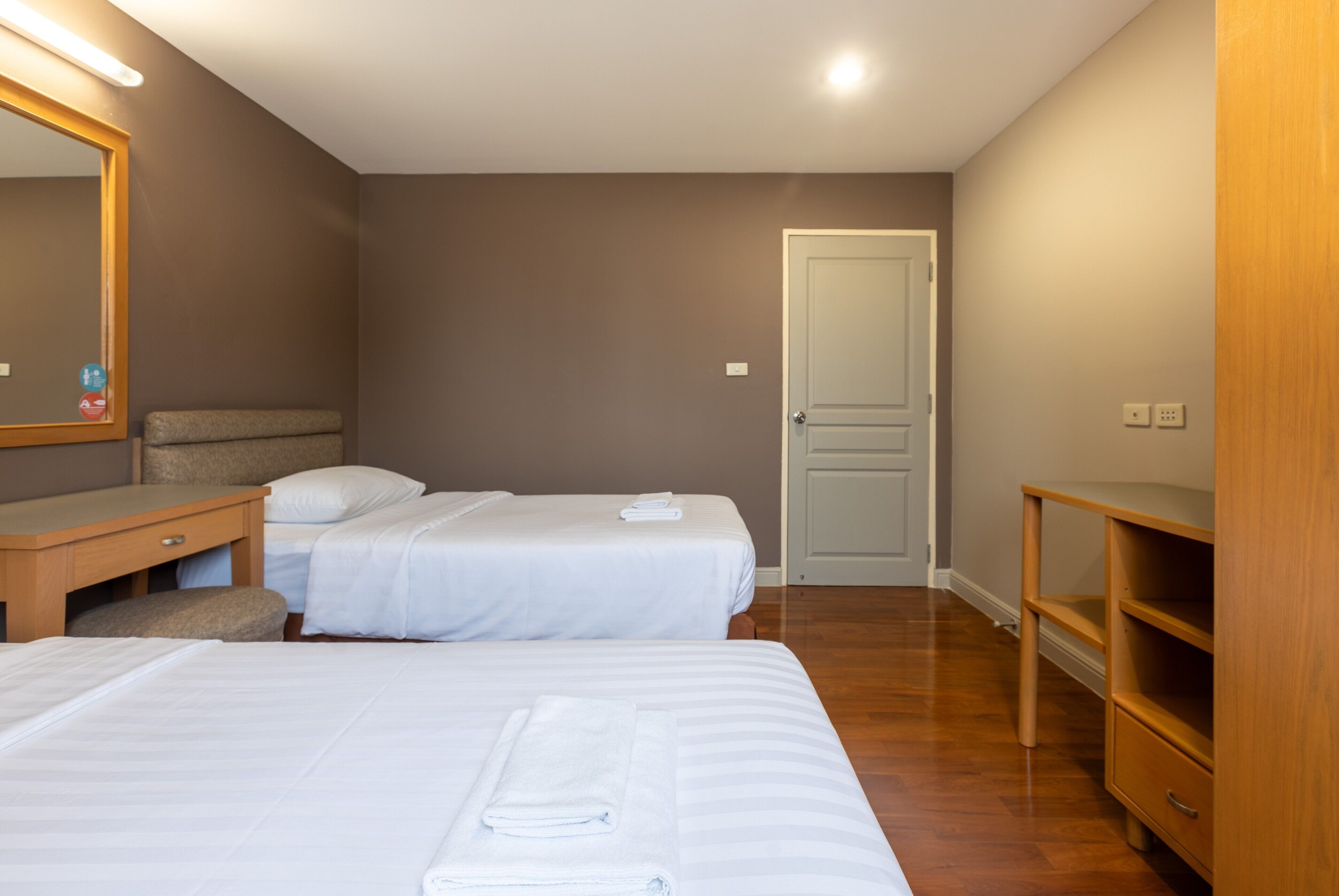 Habitación de hotel con dos camas, un escritorio, una silla, un aparador de madera y una puerta.