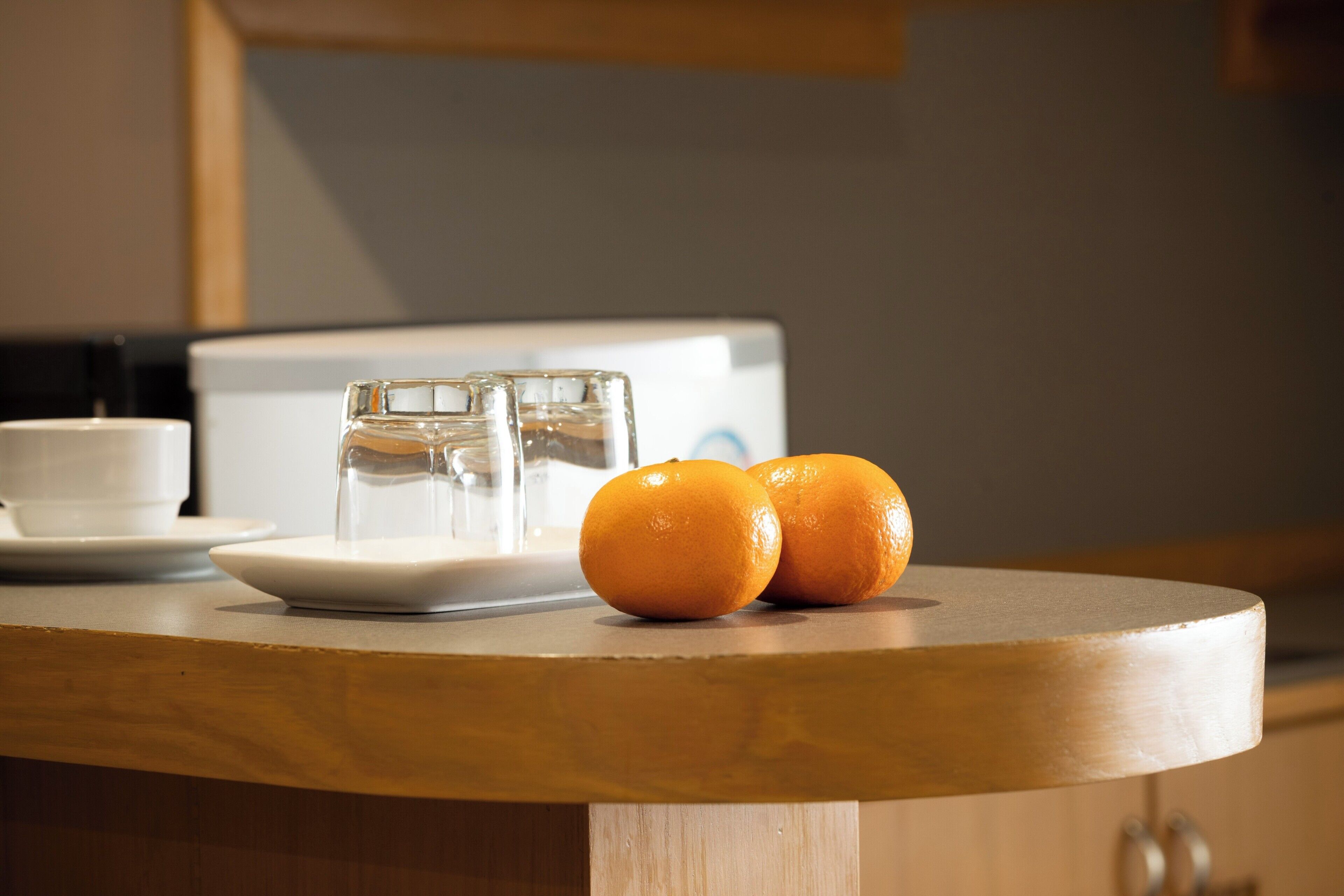 A wooden table with two oranges, a glass, and a white cup.
