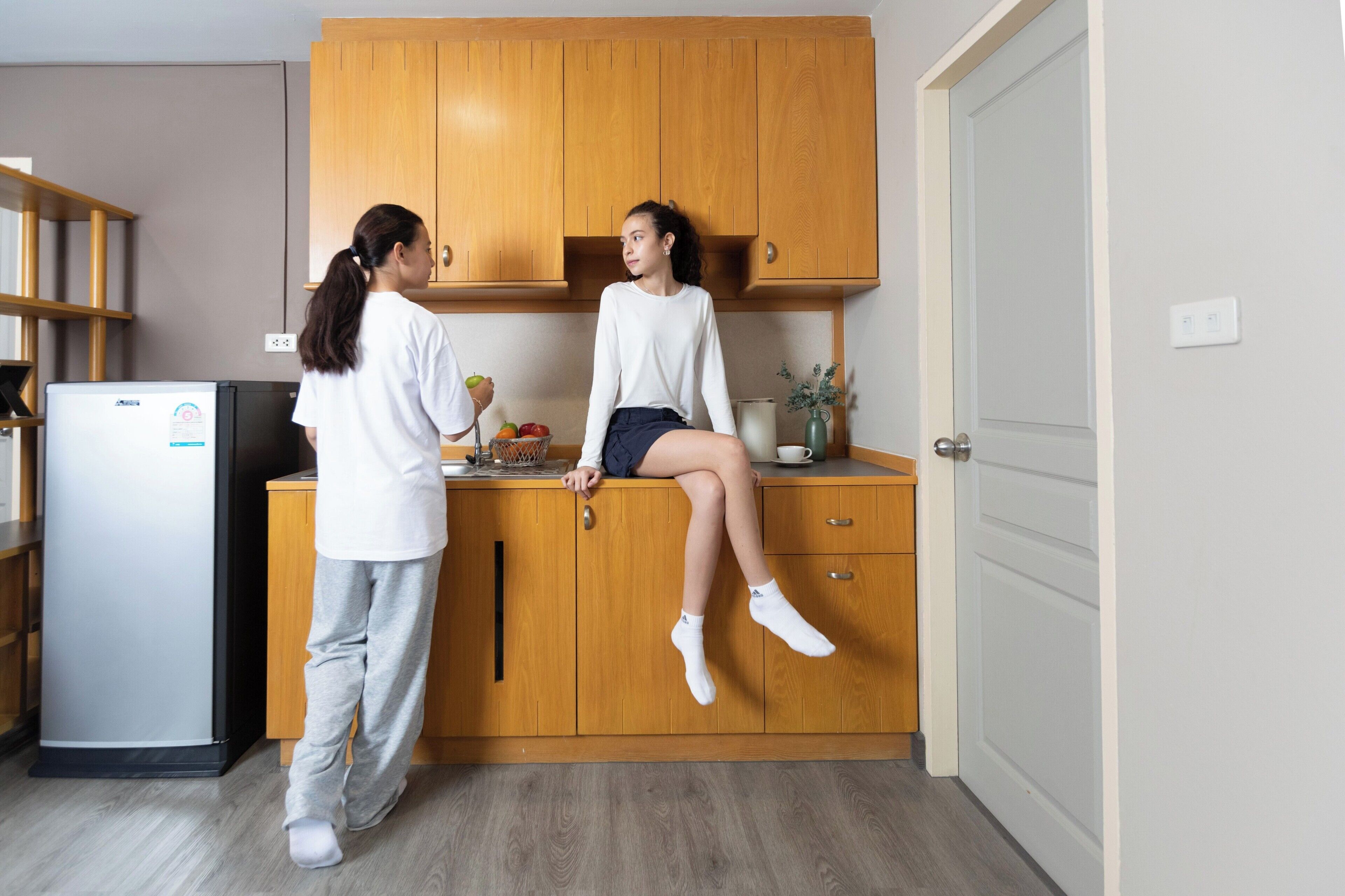 Una cocina con armarios de madera, un refrigerador y una persona de pie junto al mostrador.
