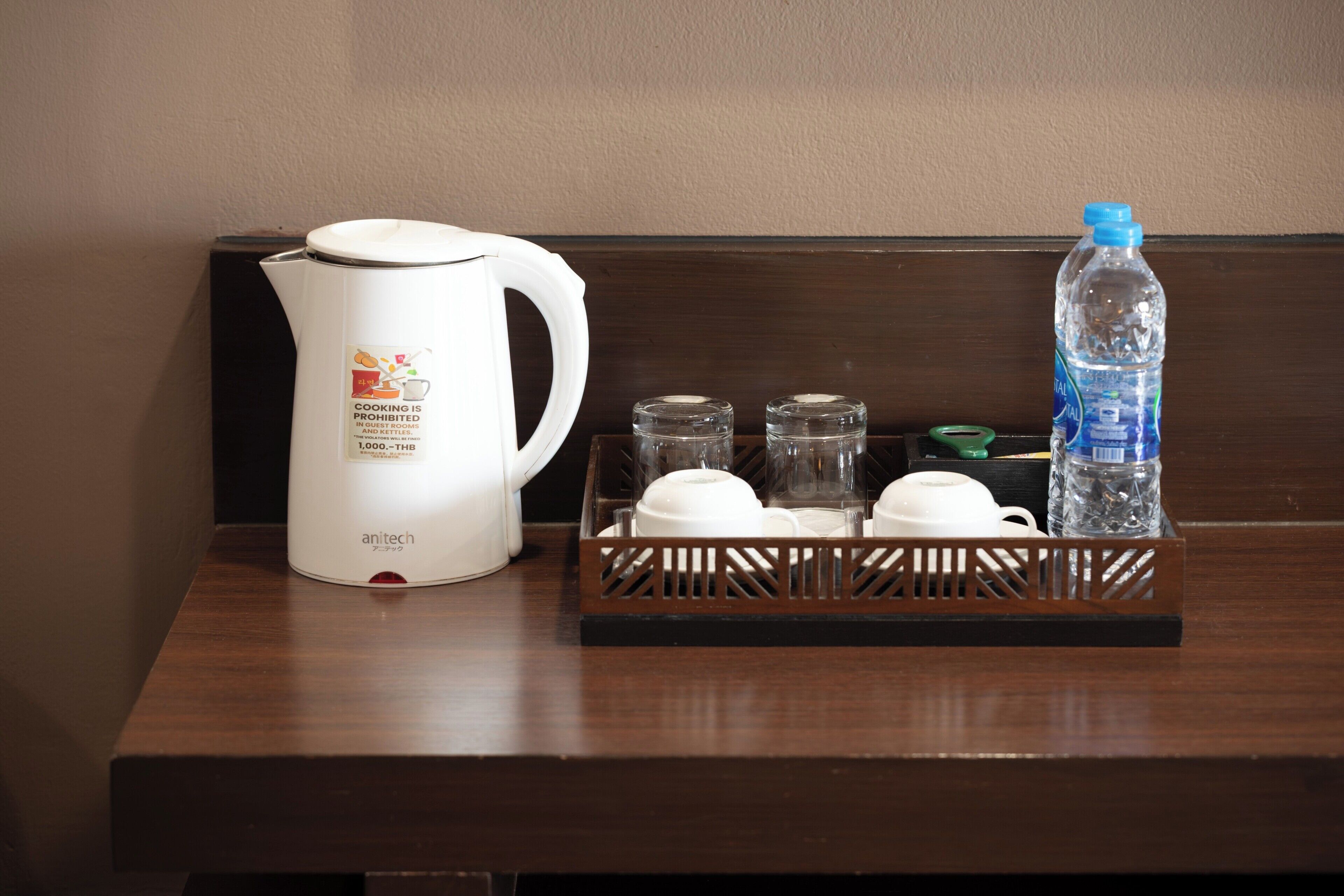 Un coin cuisine comprenant une bouilloire électrique blanche, une bouteille d’eau et un plateau avec des tasses et une théière.