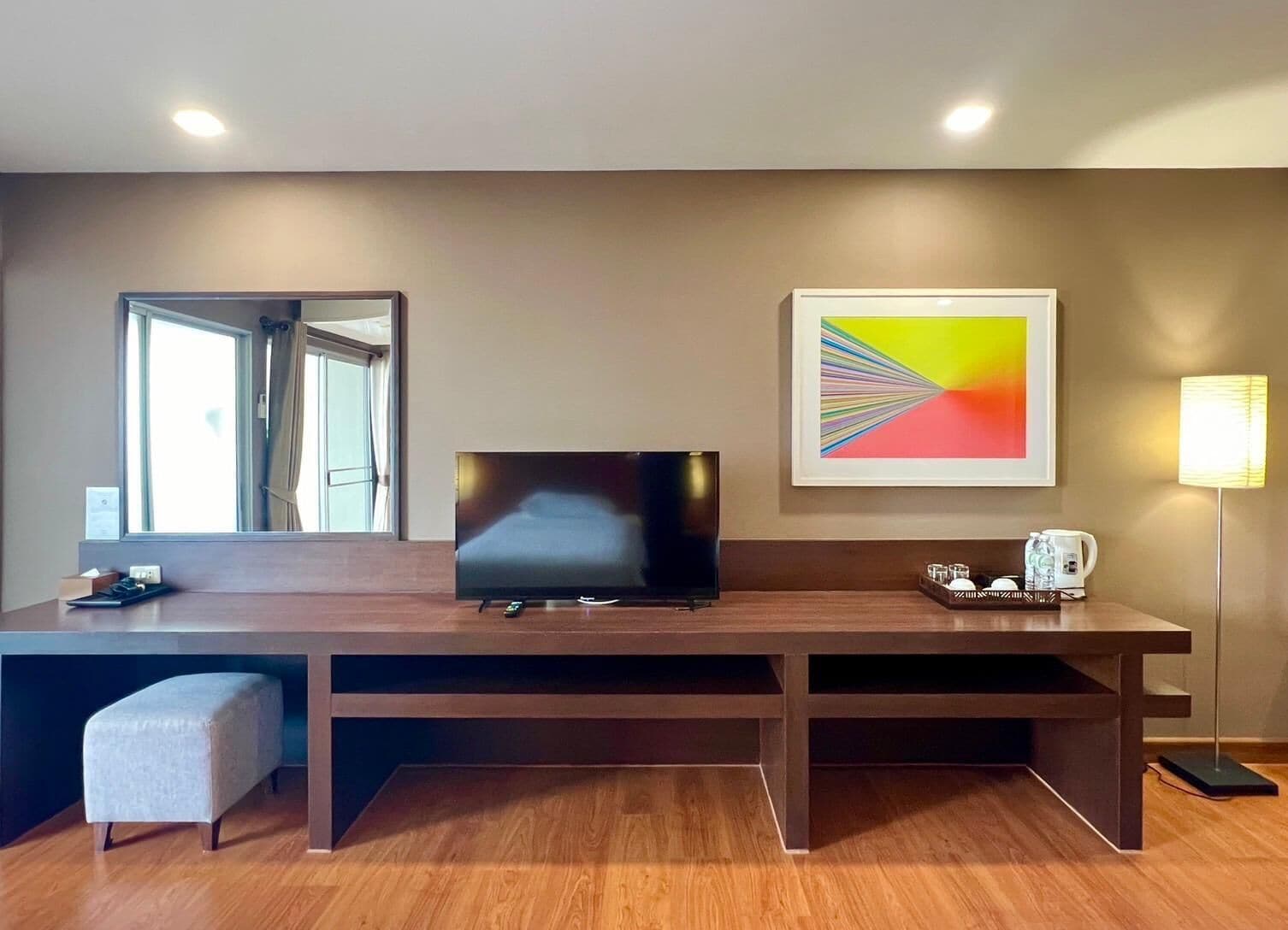 A modern hotel room with a flat-screen TV, a coffee maker, and a framed abstract painting.