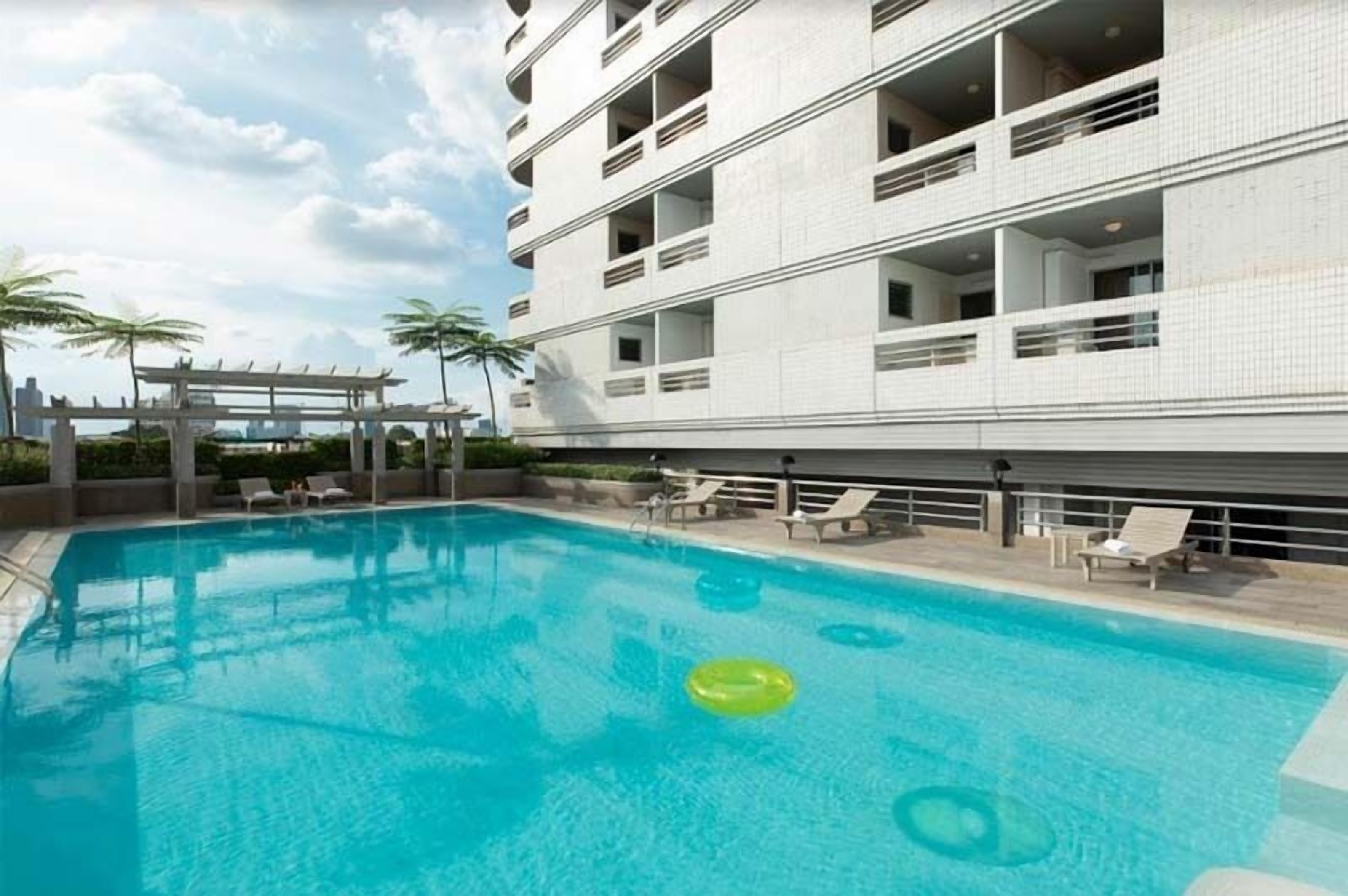 A modern hotel with a rooftop pool, lounge chairs, and a pergola.