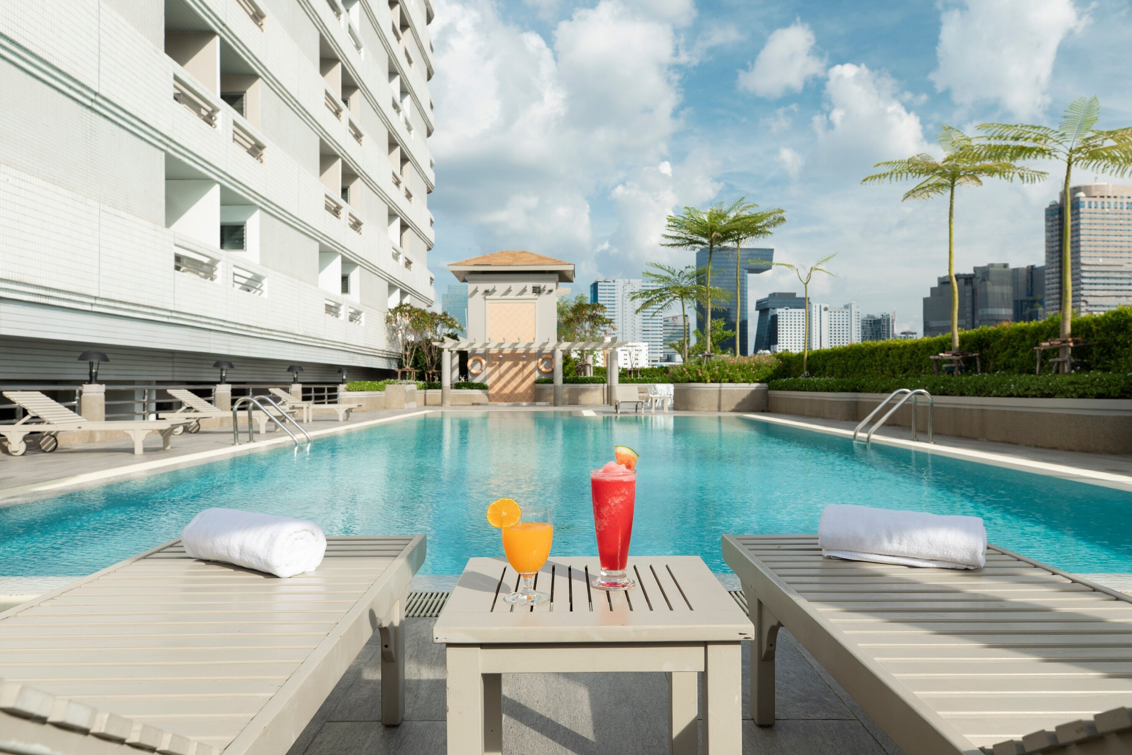 A poolside area with lounge chairs, a table with a drink, and a cityscape in the background.