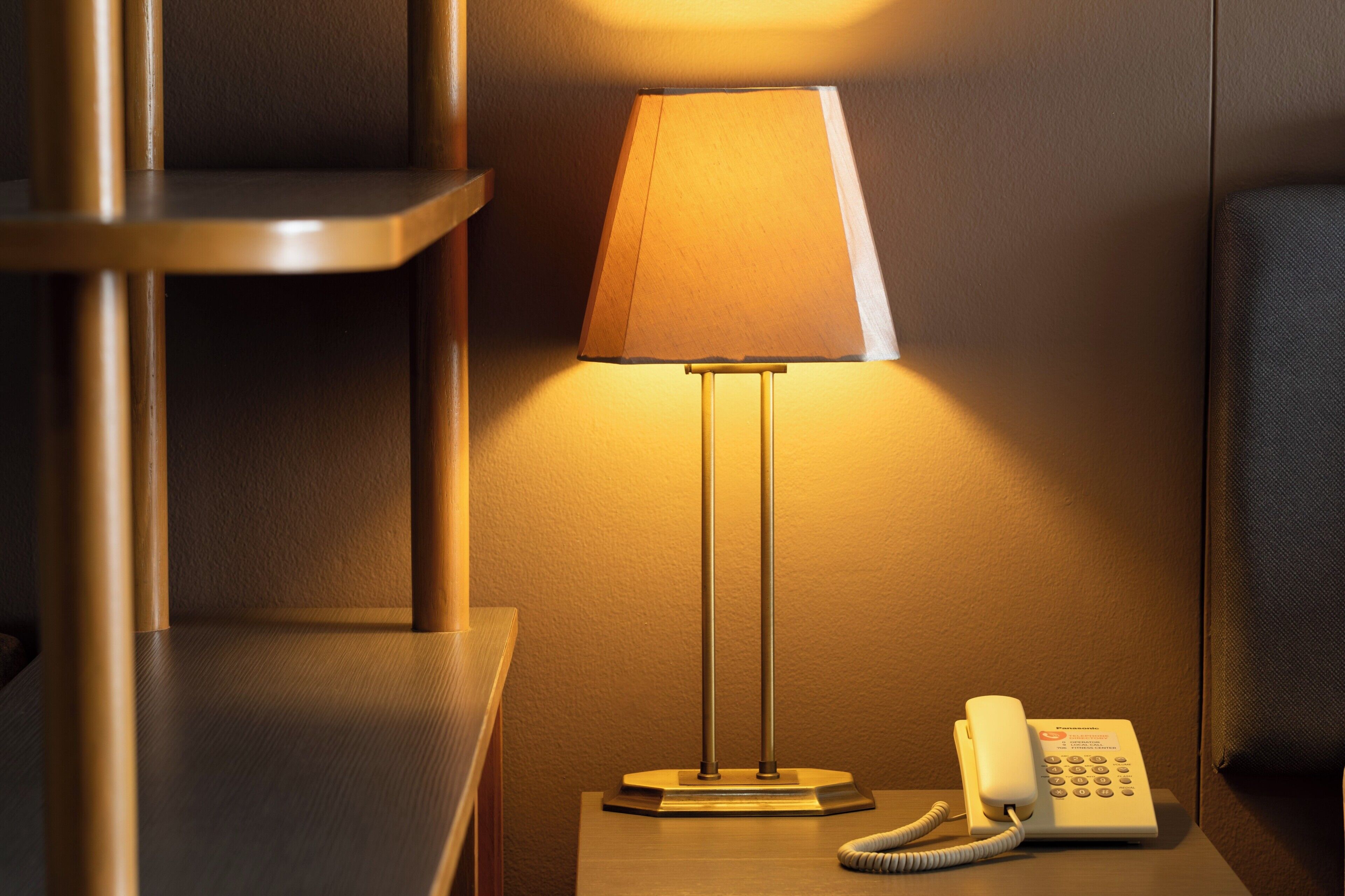 A hotel room with a bedside lamp, a telephone, and a wooden nightstand.