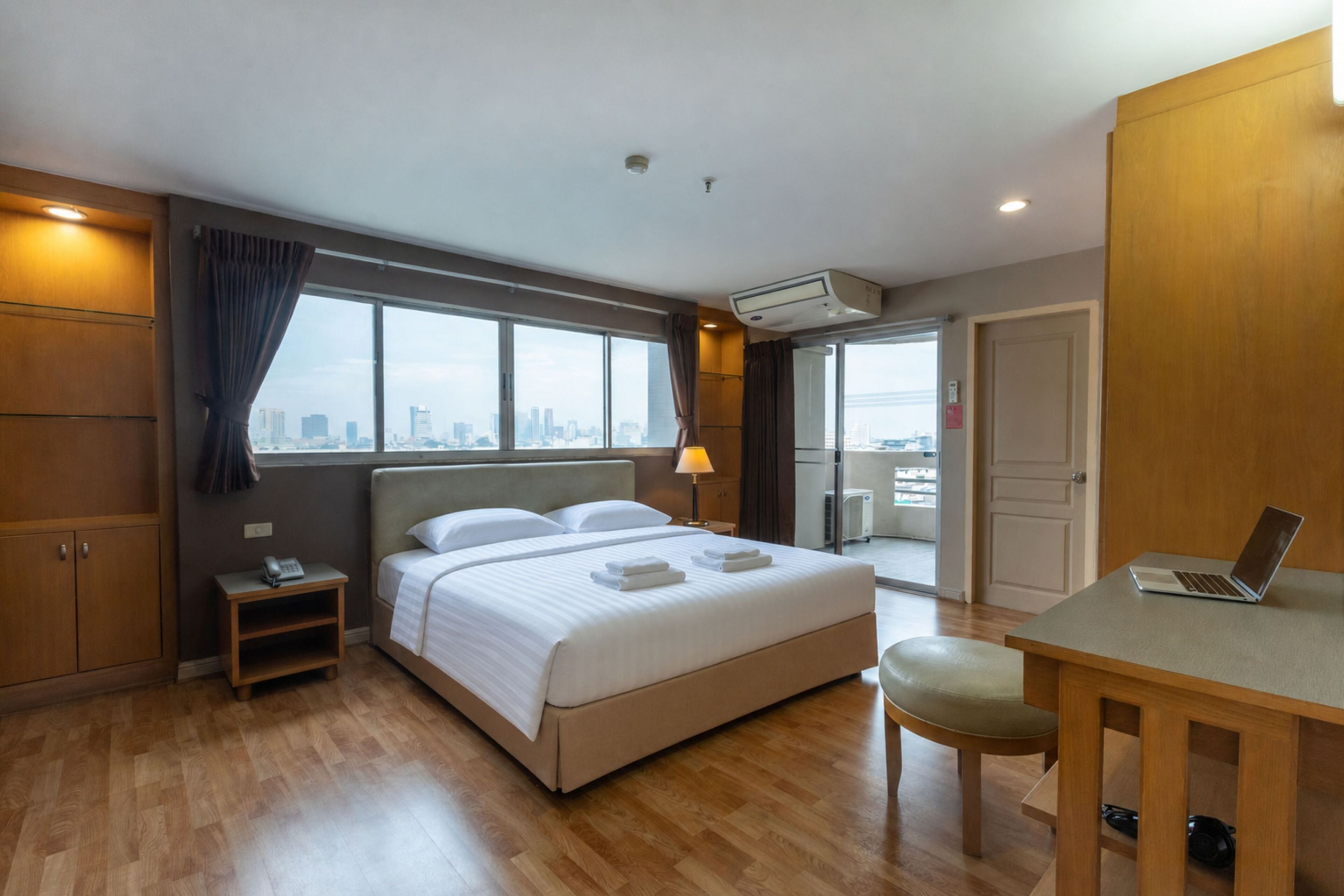 A hotel room with a bed, a desk, a chair, and a city view through the window.
