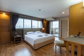 A hotel room with a bed, a desk, a chair, and a city view through the window.
