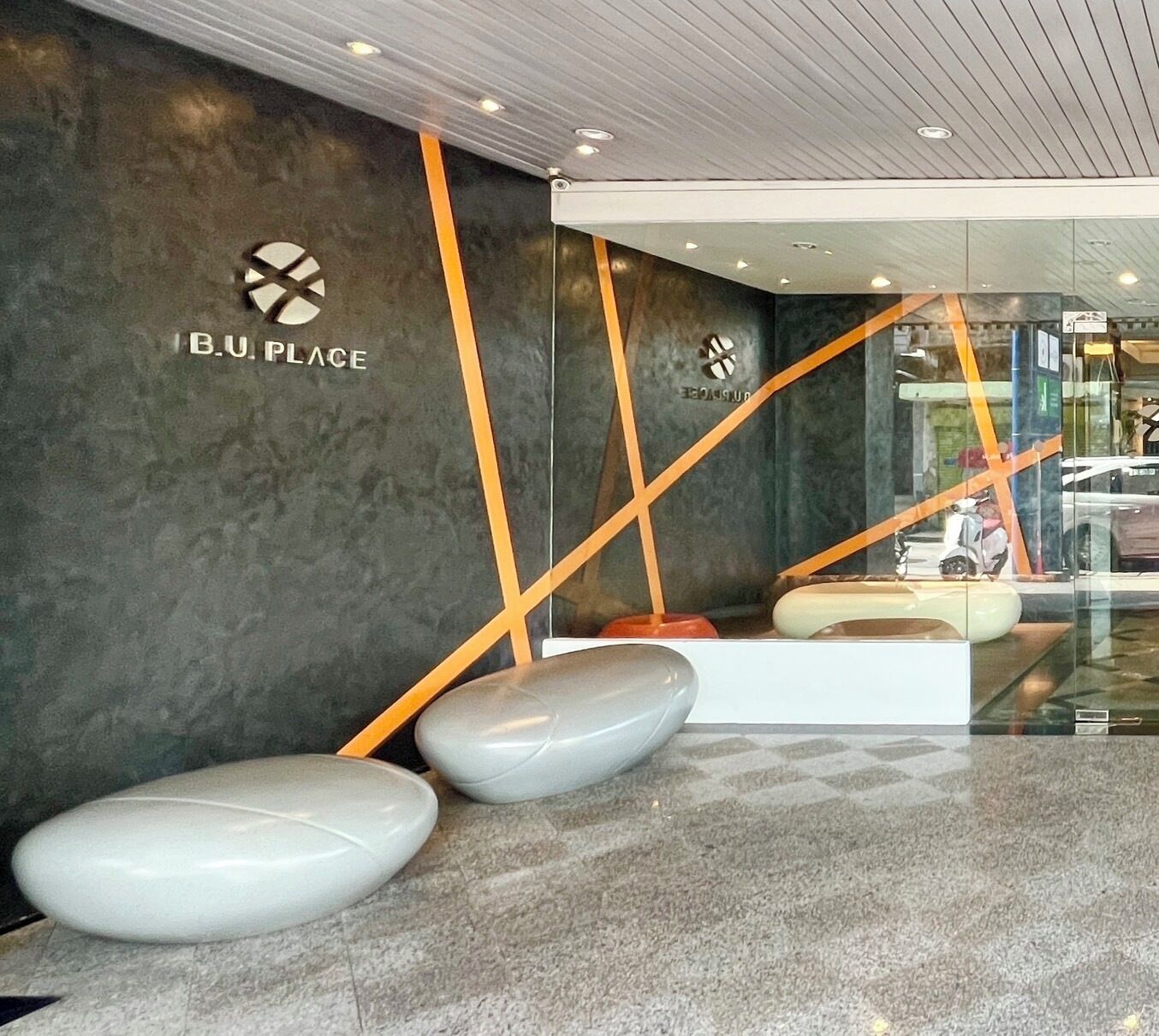 A modern interior with a dark wall, a logo, and a seating area with a glass partition.