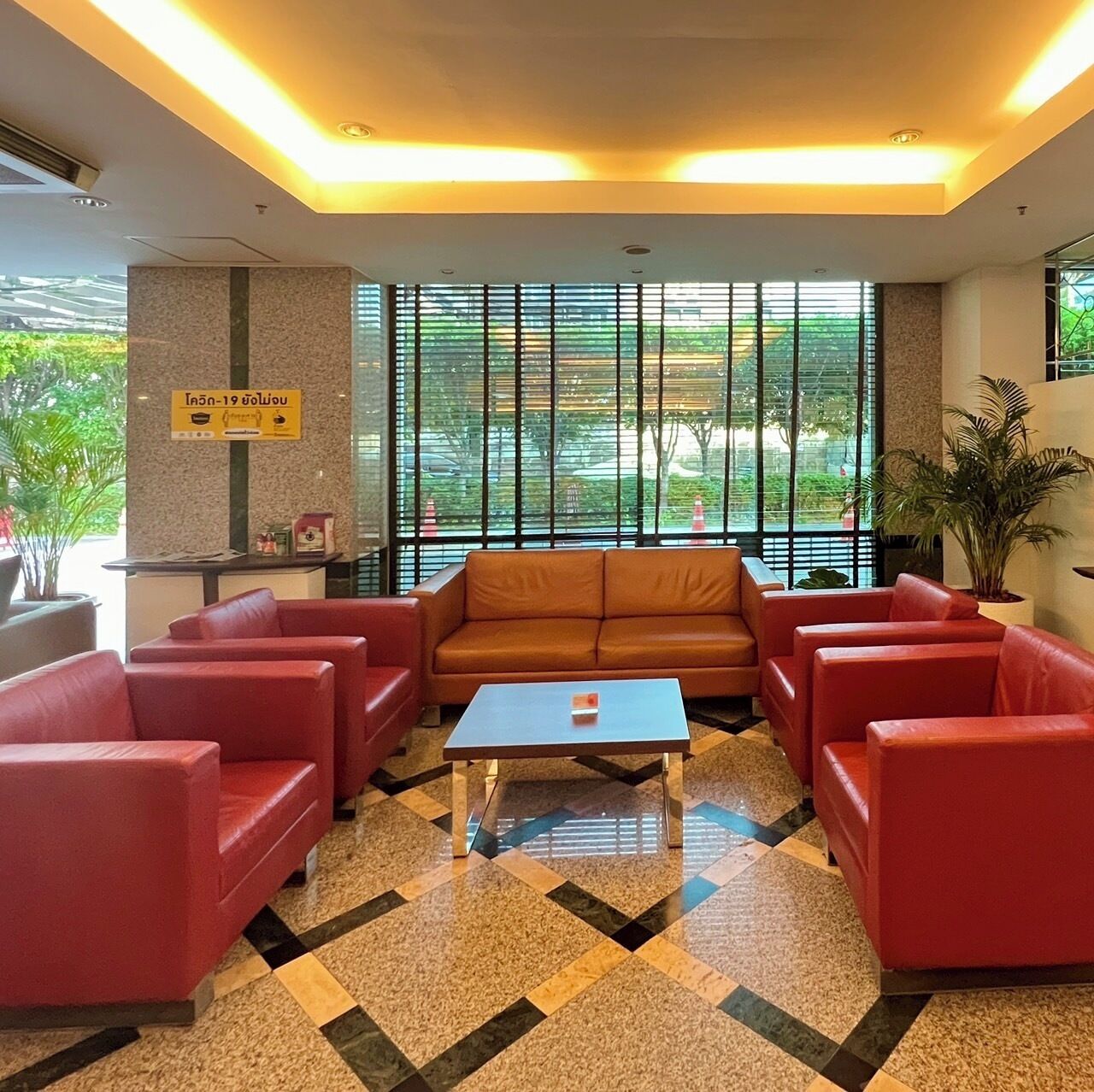 A lobby with red sofas, a central coffee table, and large windows with blinds.