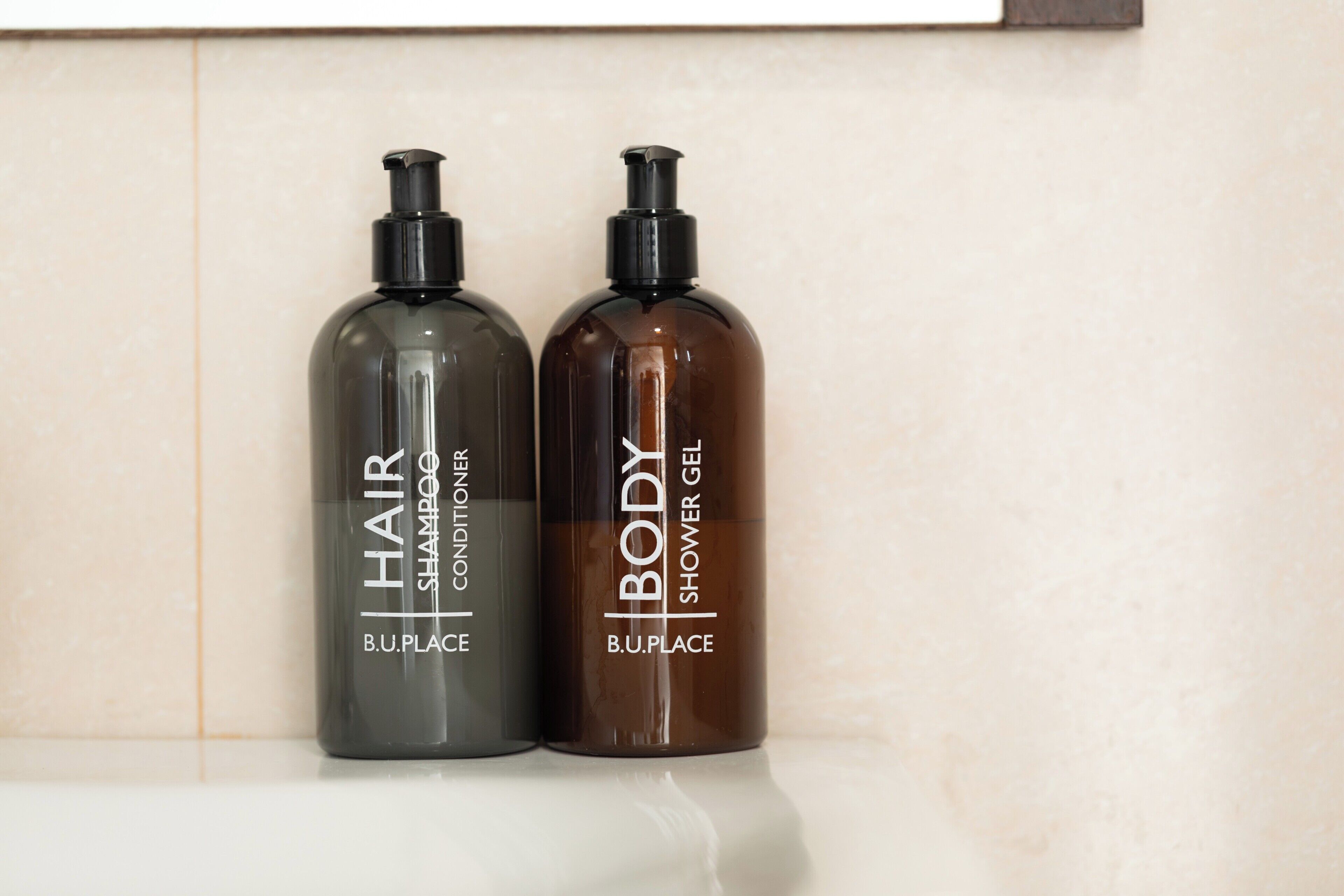 Twee flessen B.U.PLACE haarconditioner en douchegel voor het lichaam op een plank.