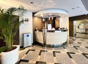 A hotel reception area with a modern design, featuring a reception desk, a clock, and a potted plant.