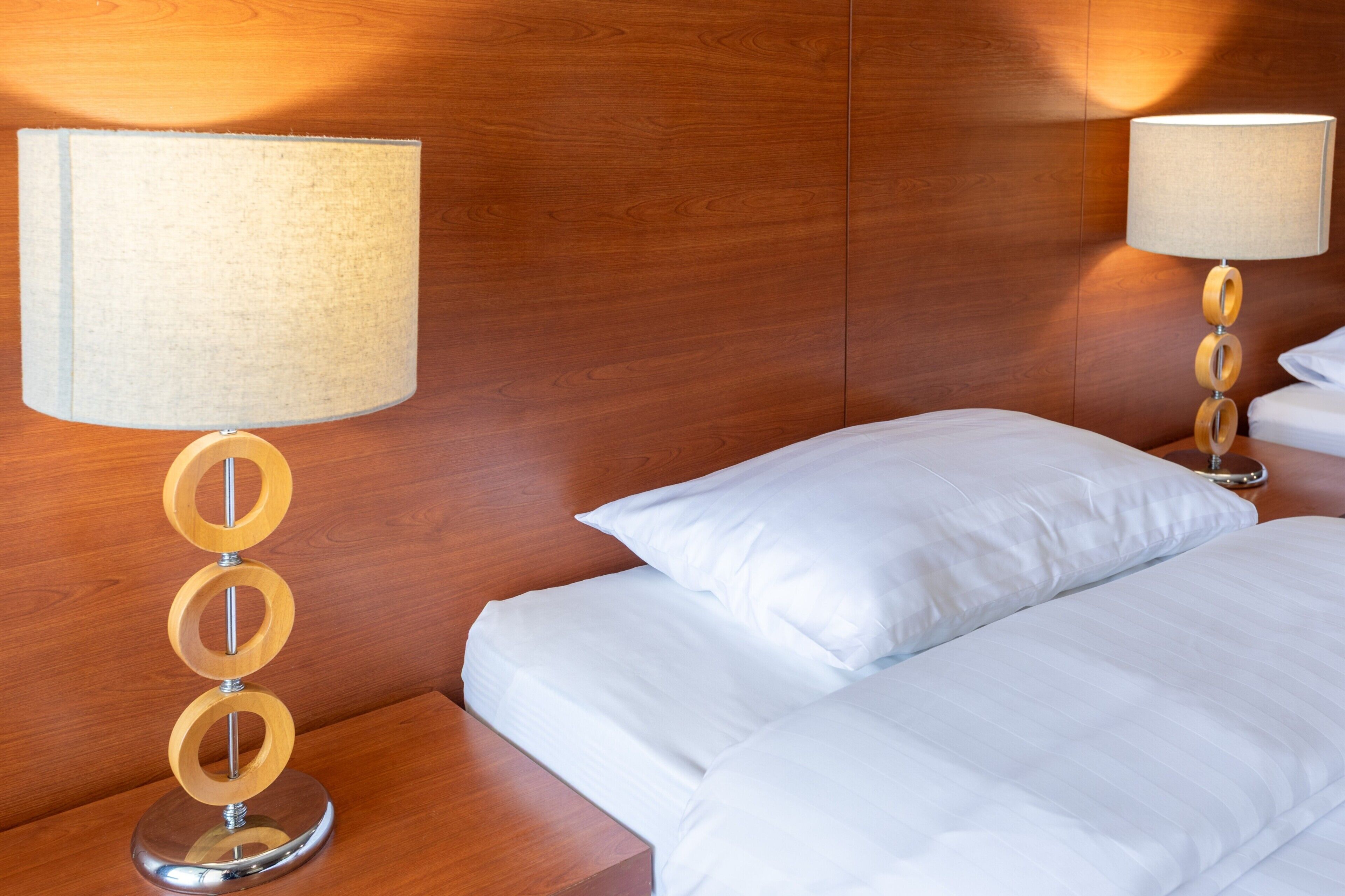 A hotel room with a wooden headboard, two bedside tables with lamps, and neatly made beds with white linens.