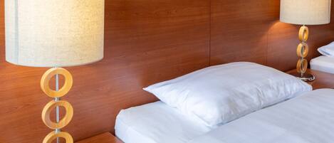 A hotel room with a wooden headboard, two bedside tables with lamps, and neatly made beds with white linens.