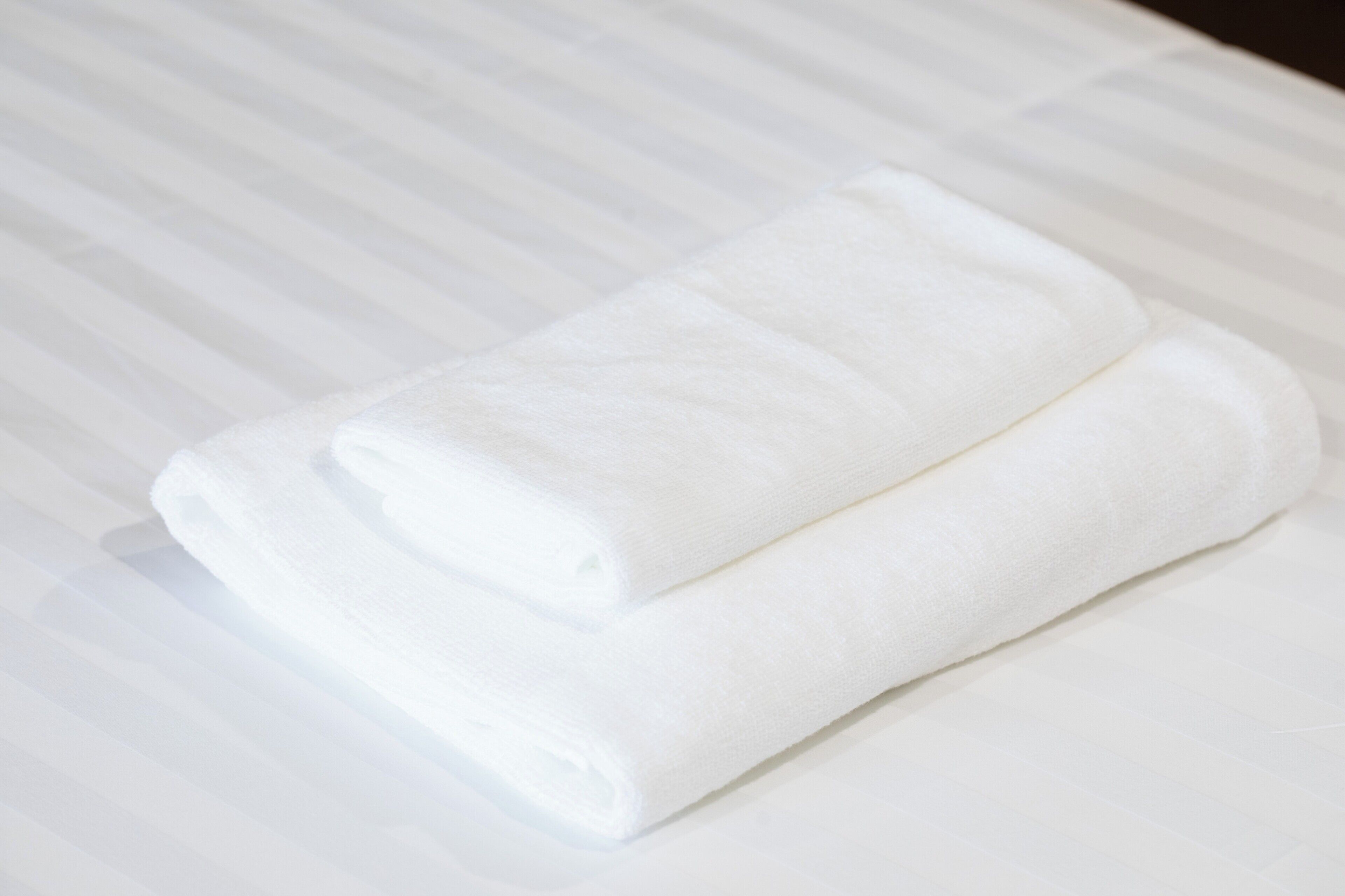 A neatly folded white towel on a bed with a striped bedspread.