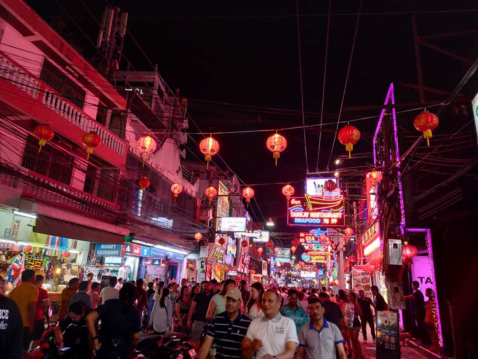 Rua movimentada à noite, com letreiros de neon e lanternas vermelhas.