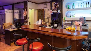 Eine Bar mit einer Holztheke, roten Barhocker und einem Flaschenregal.