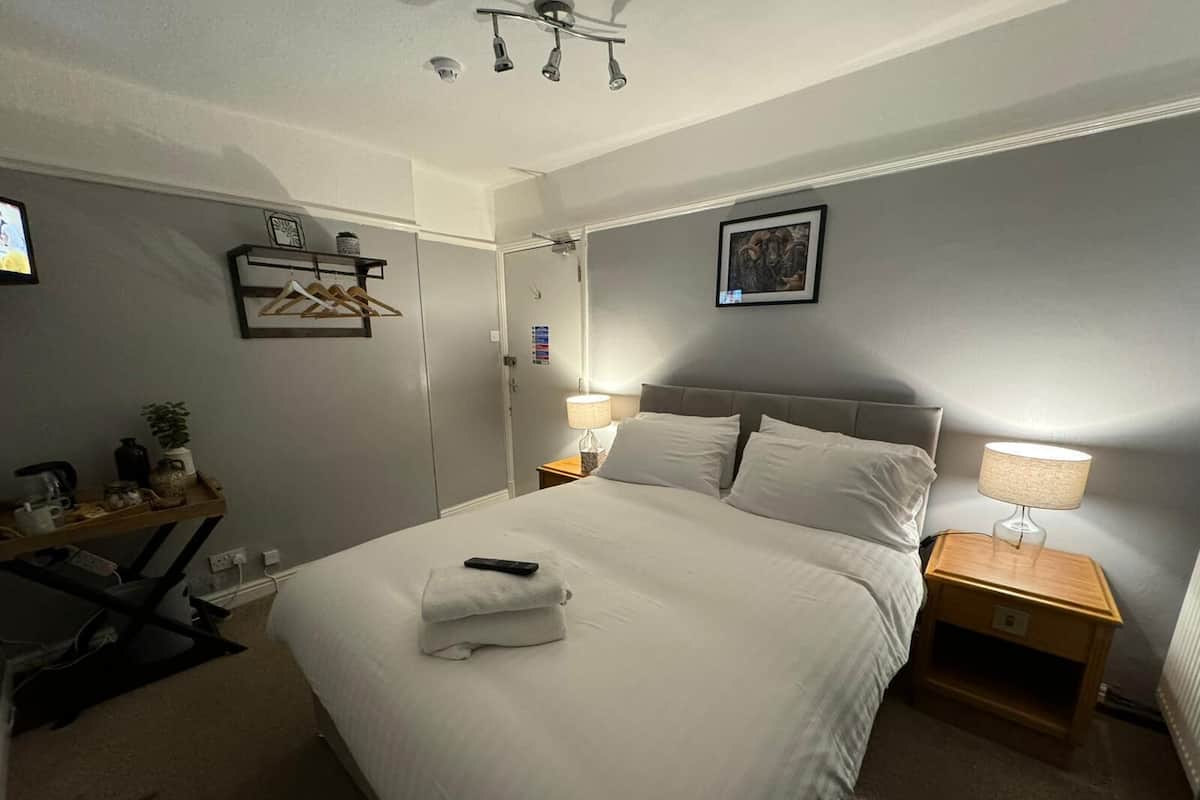 A neatly arranged hotel room with a bed, bedside lamps, a small table, and a wall-mounted shelf.