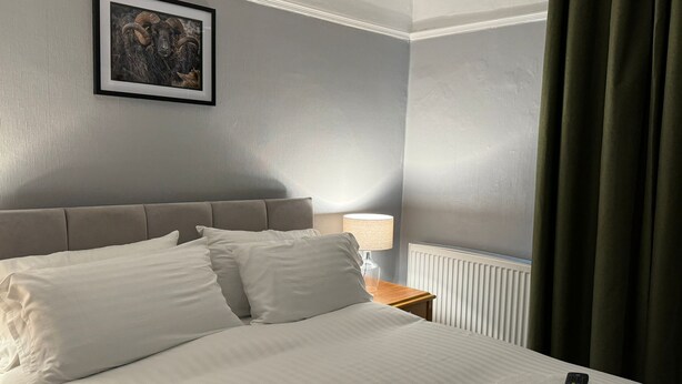 A hotel room with a bed, a framed picture on the wall, a lamp, and a remote control on the bed. - The George Hotel (Penrith)