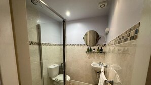 A bathroom with a glass-enclosed shower, a toilet, a sink, and a mirror. - The George Hotel (Penrith)