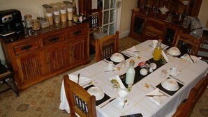 Een eetkamer met een lange tafel gedekt voor een maaltijd, houten meubels en diverse keukenspullen op het buffet.