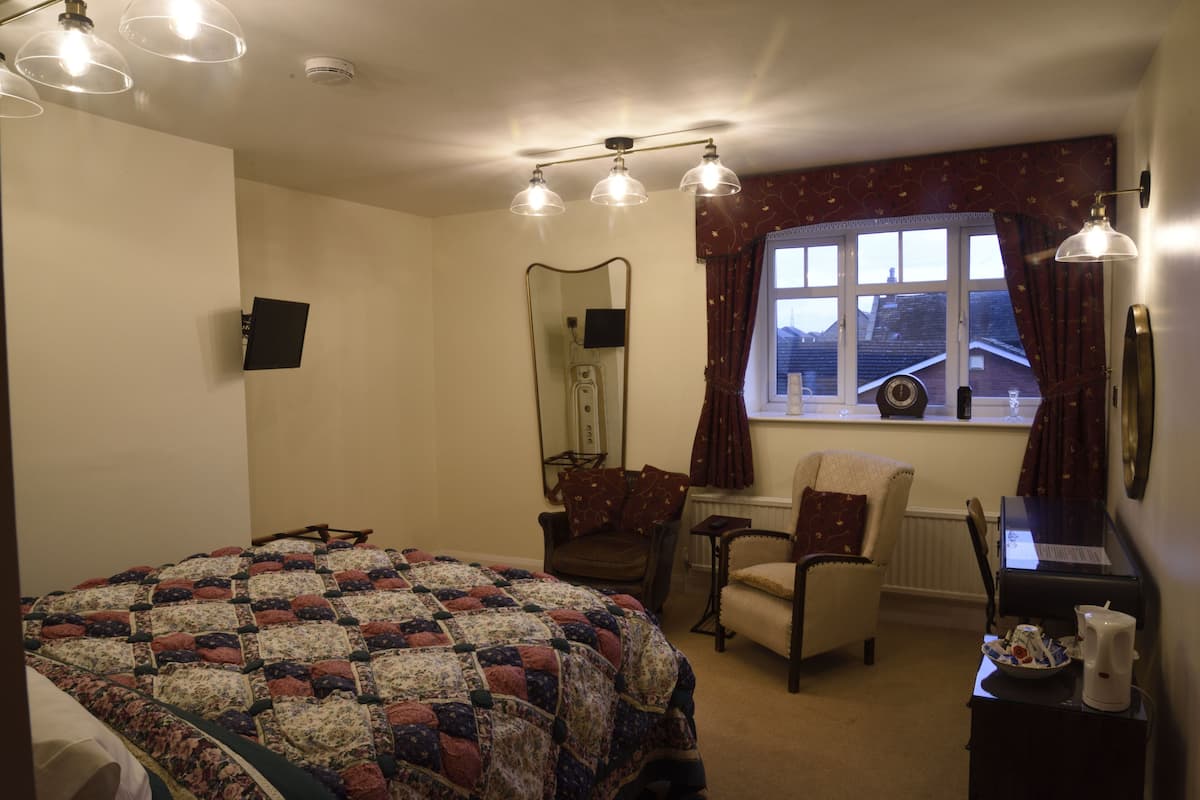 Une chambre à coucher avec un grand lit, un bureau, une chaise, un miroir et une fenêtre avec des rideaux.