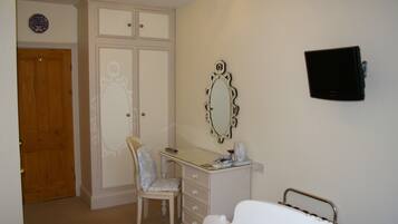A bedroom with a bed, a desk, a chair, a wardrobe, and a television.