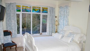 Een slaapkamer met een bed, een stoel, een nachtkastje, een lamp en een raam met gordijnen.