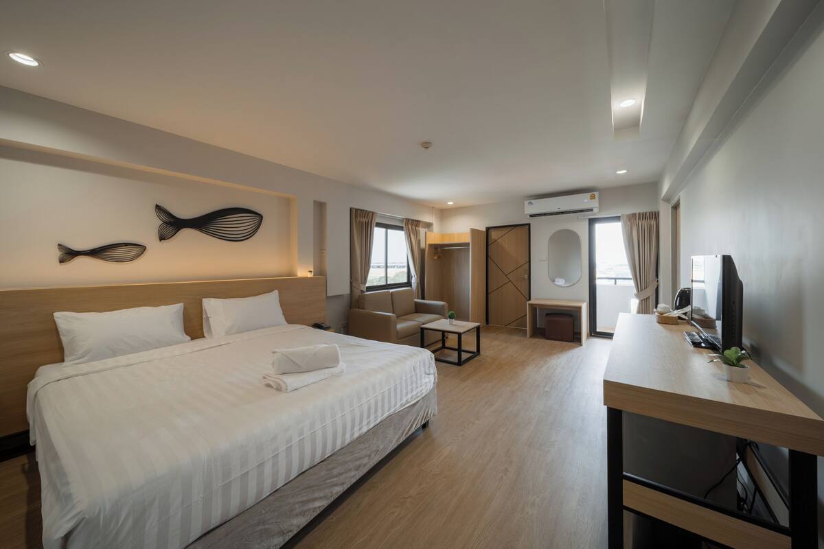 A hotel room with a large bed, a desk with a computer, a TV, and a window with curtains.
