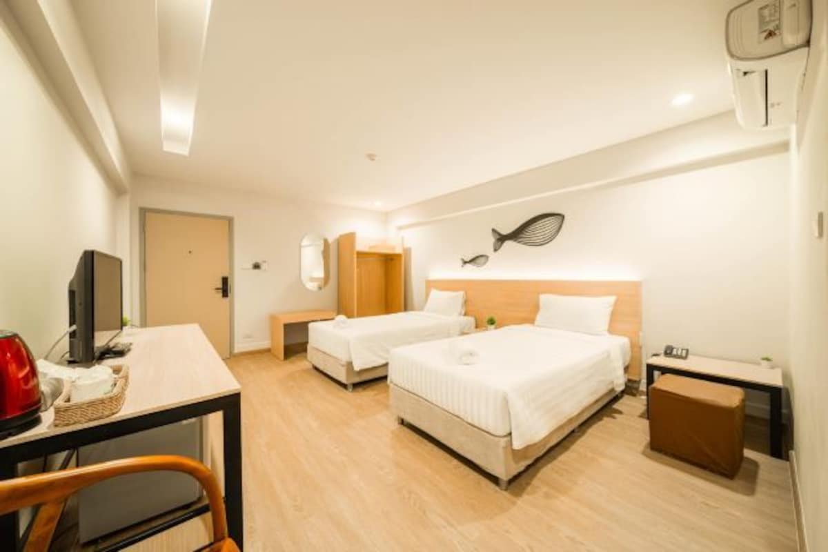 A hotel room with two beds, a desk with a TV, a small table, and a wall-mounted heater.