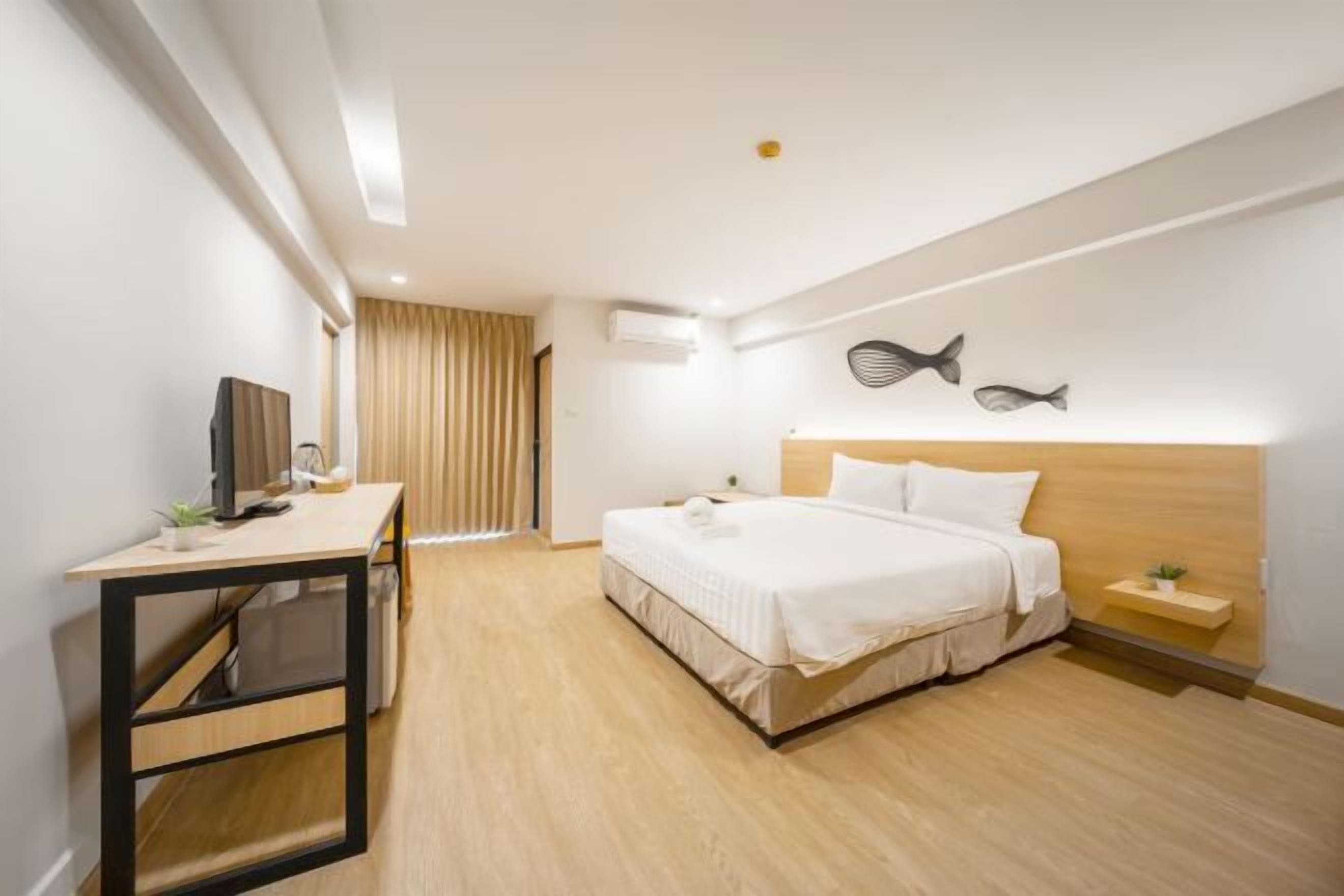 A modern hotel room with a bed, a desk, a TV, and a wall-mounted fish decoration.