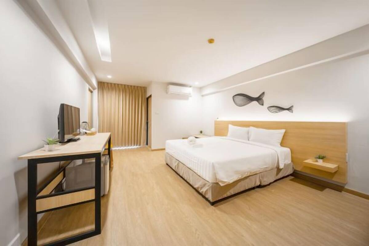 A modern hotel room with a bed, a desk, a TV, and a wall-mounted fish decoration.