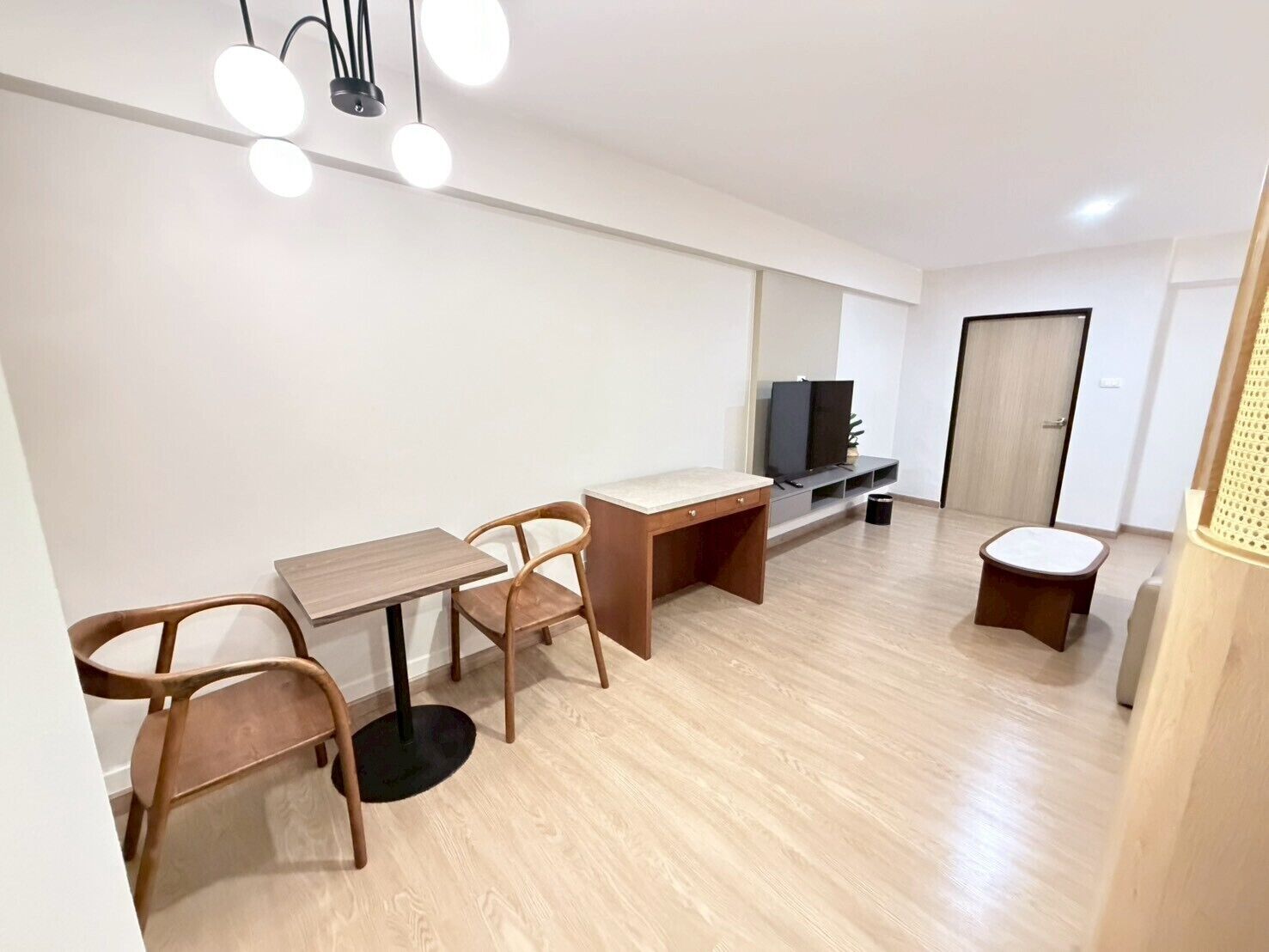 A modern living room with a wooden floor, a dining table with chairs, a TV stand, and a door.