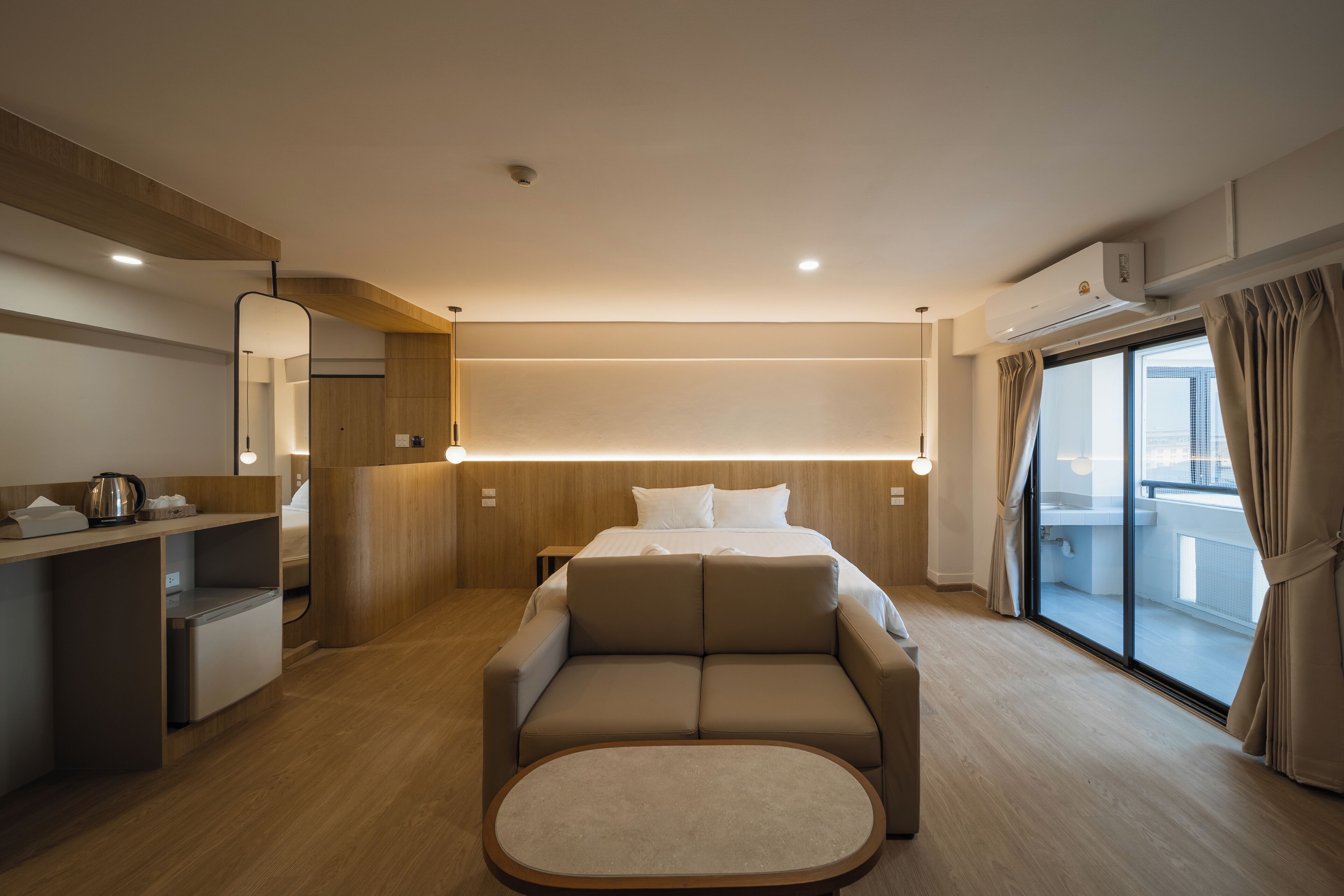 A modern hotel room with a bed, a sofa, a small desk, and a balcony with curtains.