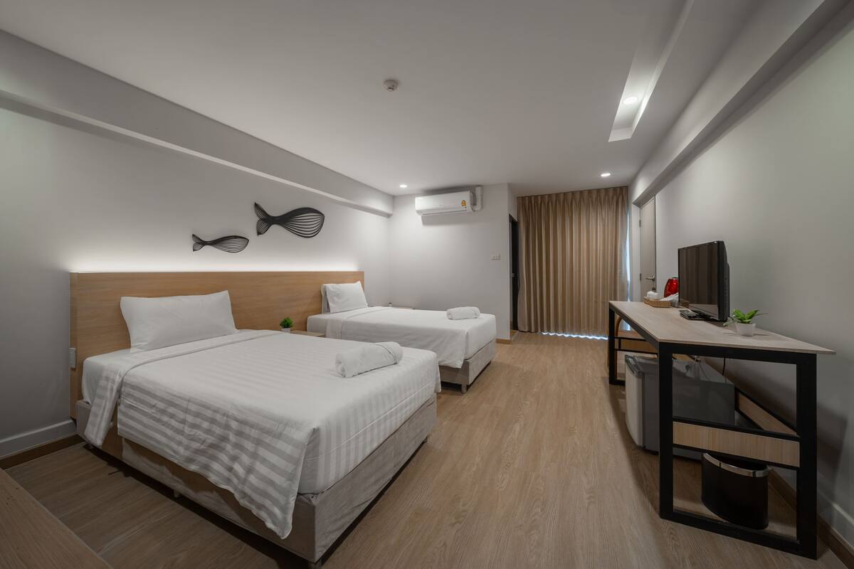 A hotel room with two beds, a desk, a chair, a TV, and a small trash bin.