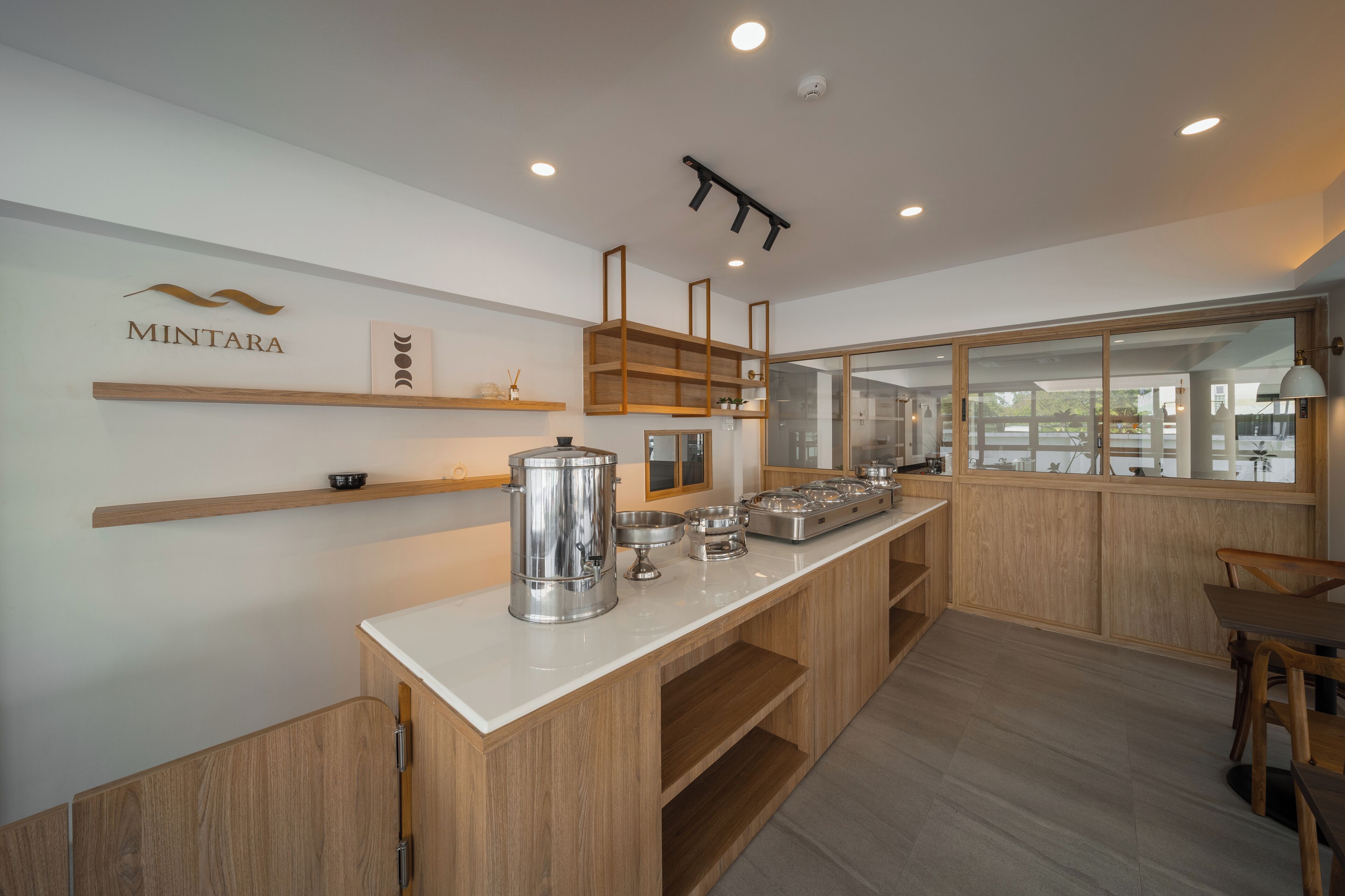 Una cocina moderna con armarios de madera, encimera blanca y electrodomésticos de acero inoxidable. Hay estantes de madera sobre la encimera y una ventana con vistas al exterior.