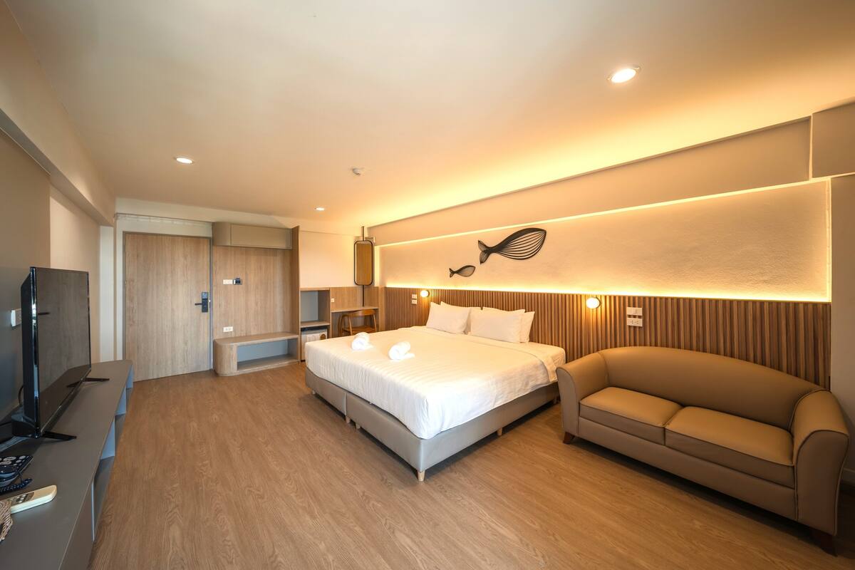 A modern hotel room with a large bed, a sofa, a TV, and a wooden floor.